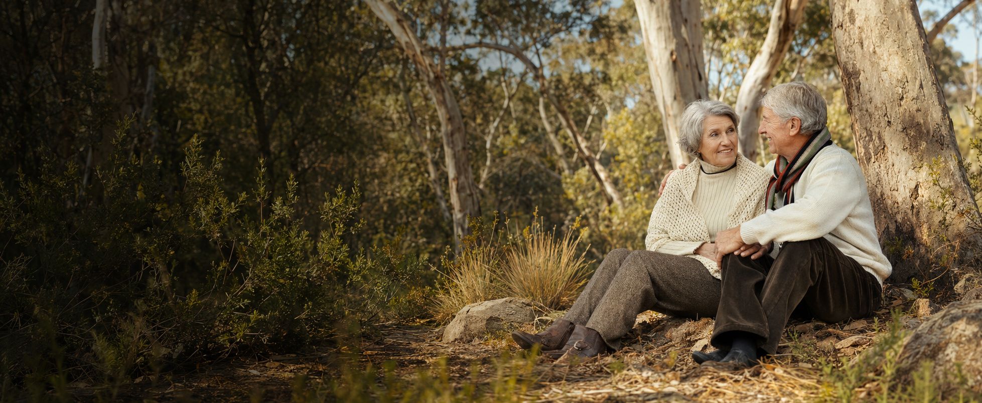 An older couple sitting together and talking outdoors among autumn trees